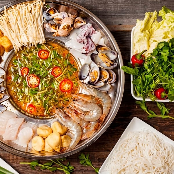 A hot pot with various seafood, mushrooms, tofu, and vegetables on a wooden table.