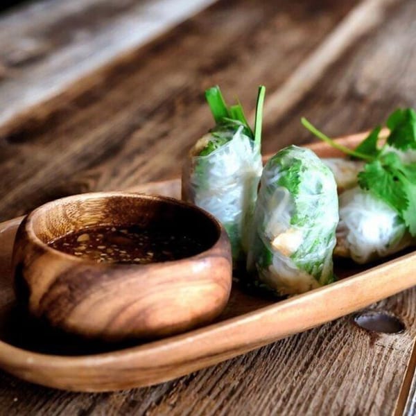 Fresh spring rolls with cilantro and a side of dipping sauce in a wooden bowl.
