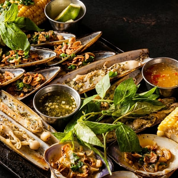 A platter of grilled seafood, including razor clams, mussels, and corn on the cob.