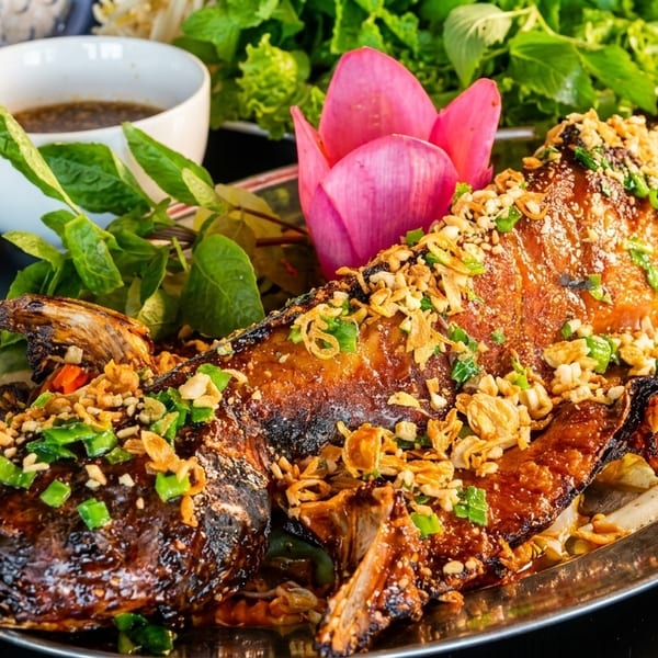 Whole grilled fish topped with peanuts and scallions, served with herbs, noodles, and sauce.